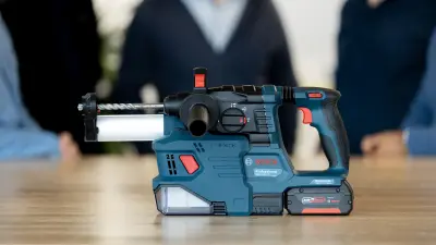 The GBH 18V-22 Professional cordless rotary hammer stands on a wooden table, with the outlines of people in the background.